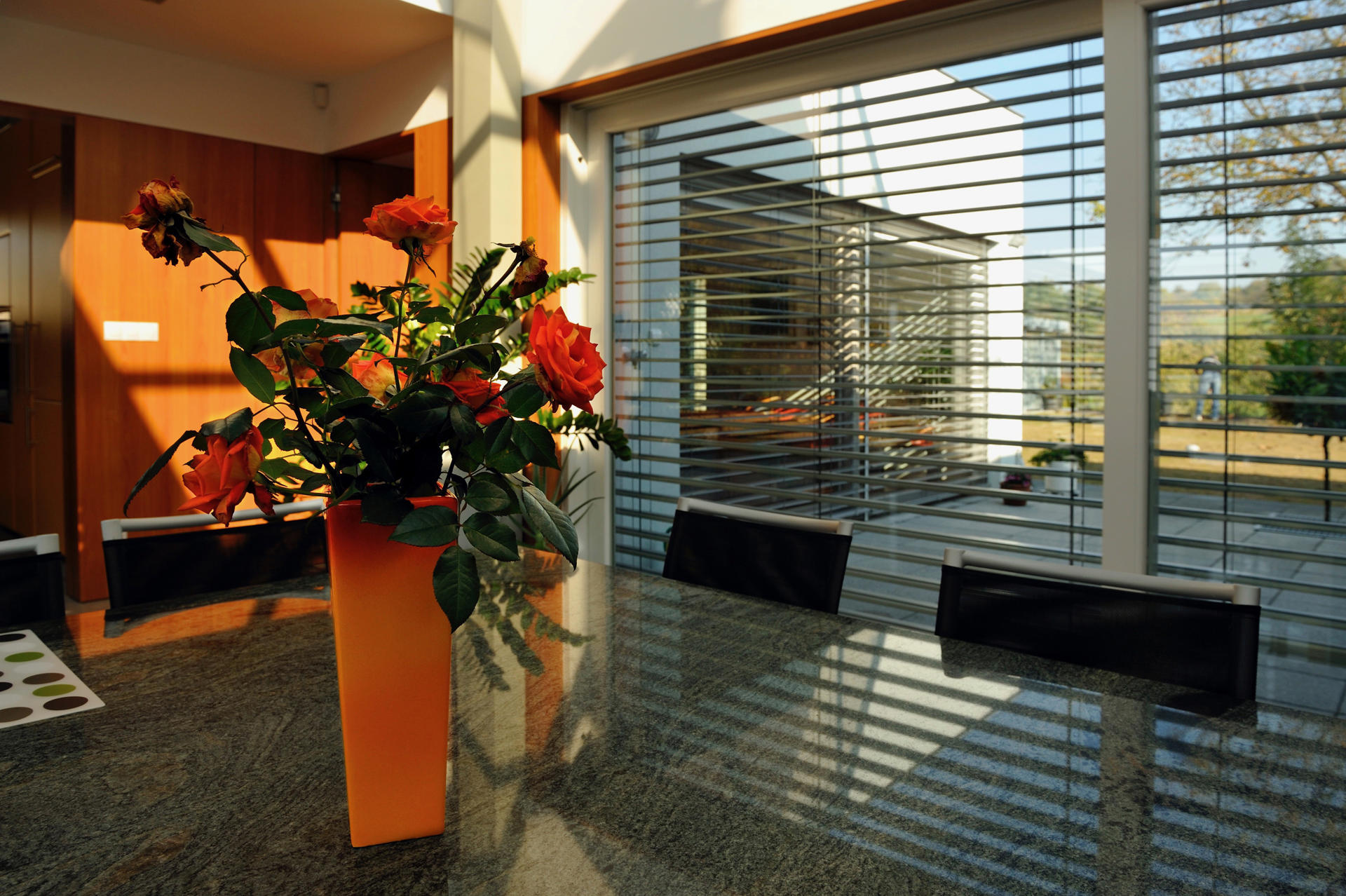 Váza s ružemi na stole a za ní okno s venkovními žaluziemi